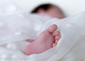 DETAILAUFNAHME EINES BABYFUSSES AUF HELLEM STOFF BEI NATÜRLICHEM LICHT