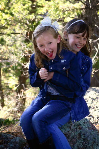 2 girls sitting on rock with younger sitting on older's lap, trees in background, outside in nature, colorado, family photography, child photography