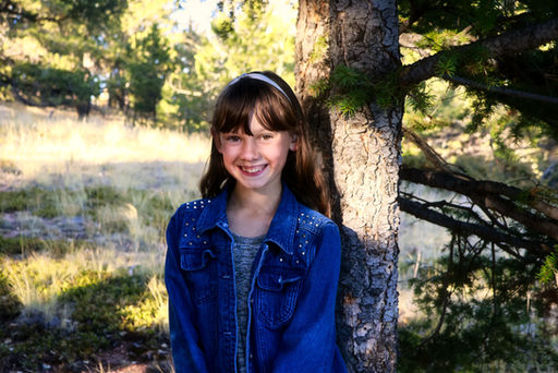 Daughter standing in front of tree with field and trees in background, smiling at camera