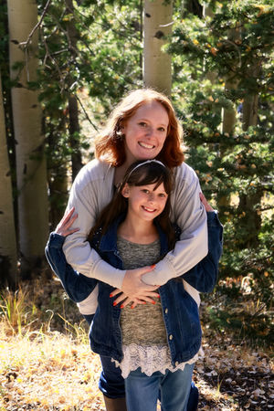 mom holding daughter in front of her, daughter holding moms arms, trees, grass in background, colorado mom and daughter photography