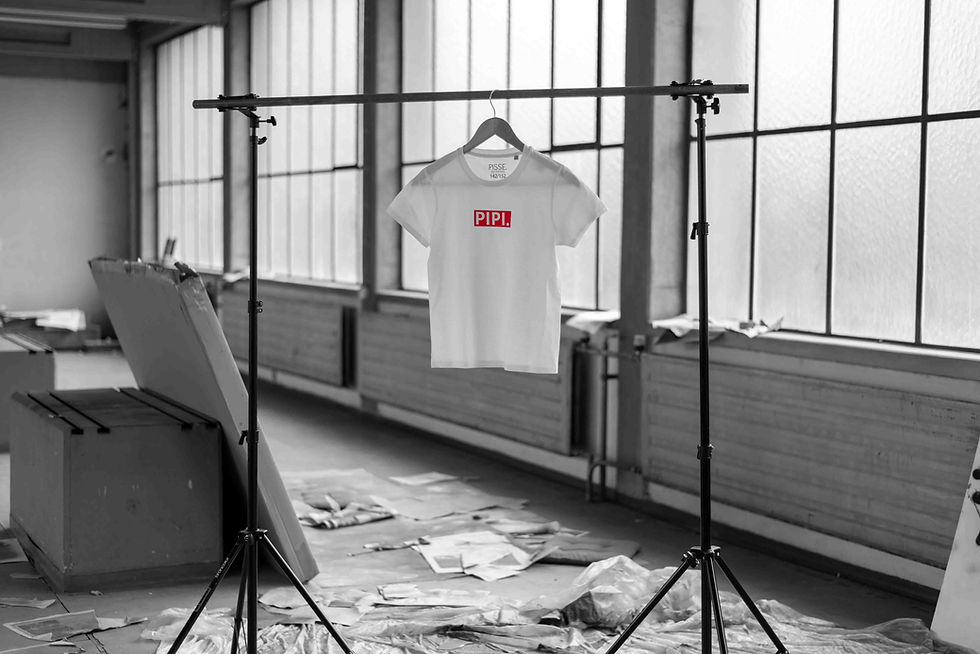 Miniaturbild: Ein weißes Shirt für Kinder mit der Aufschrift "PIPI." hängt in einer Lagerhalle.