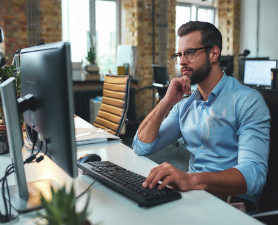 Man in blue shirt thinking at his desk in front of computer