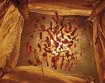 Selbstgebauter Räucherofen aus Holzstangen, Plane und Drahtgitter, in dem Fleischstücke über Feuer und Rauch getrocknet