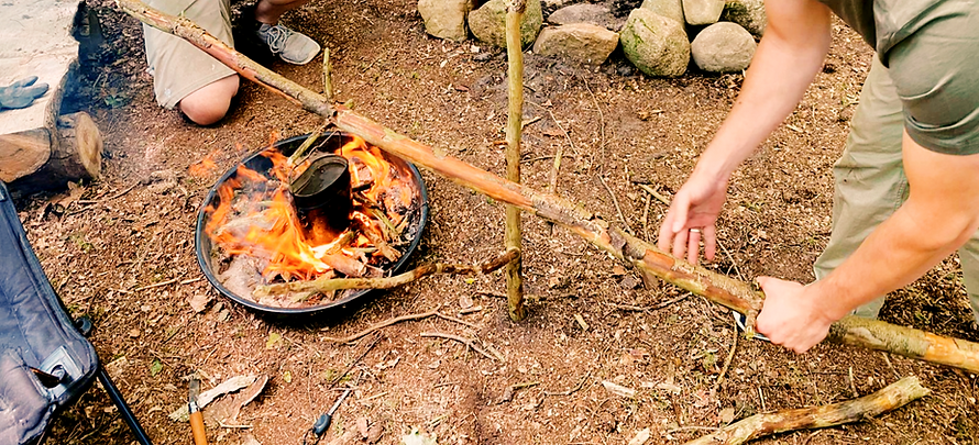 Teilnehmer kochen während eines Survivaltrainings am offenen Feuer im Wald.