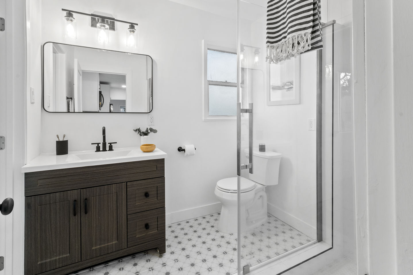 a mid century bathroom with a black vanity, horizontal curved mirror, glass corner walk-in shower