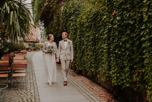 Brautpaar spaziert Hand in Hand, glücklich lächelnd, HOCHZEITEN, grüne Hecke, Hochzeitsfotograf Thüringen.