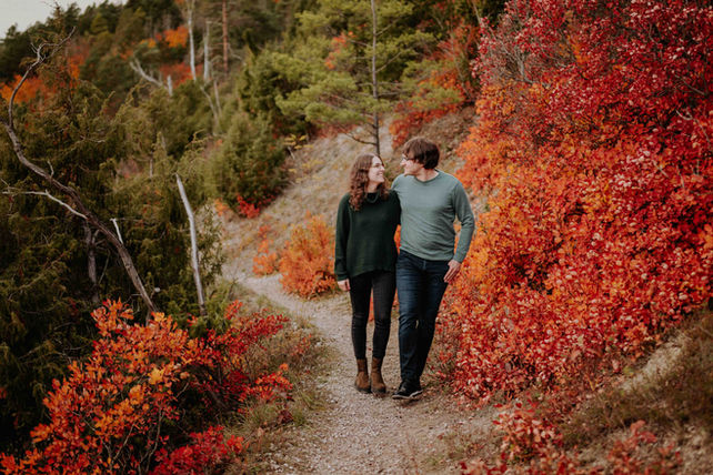Ein Paar läuft Arm in Arm zwischen herbstlichen Perückenbüschen in Jena einen Weg entlang