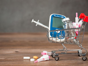 A miniature shopping cart containing diabetes-related medical equipment—glucometer, insulin vial, syringe, lancets, and tablets—symbolizing modern diabetes care and treatment choices.