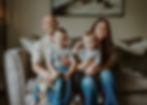 Family of four sitting on a sofa, holding their children and smiling at the camera