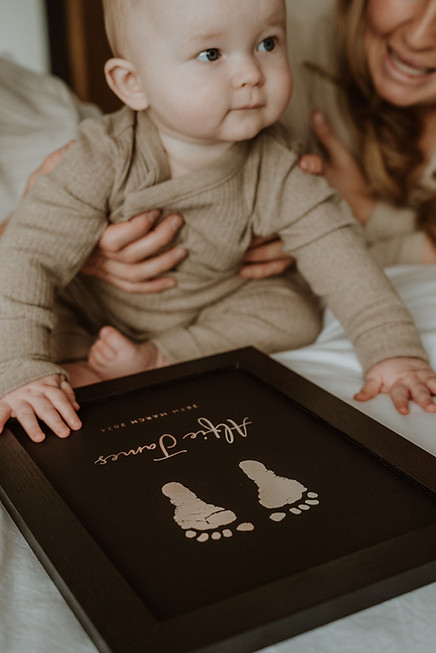 Parents with baby looking at framed foil footprint keepsake on bed