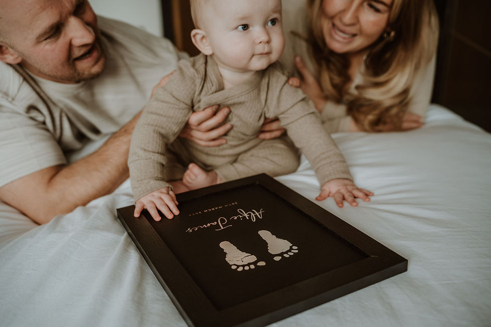 Parents with baby looking at framed foil footprint keepsake on bed