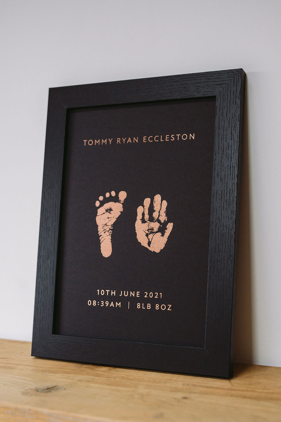 Close-up of framed black foil print featuring baby handprint and footprint