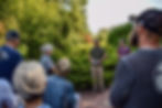A group of staff and volunteers listen to Cara Lawson-Ball in a lush garden. The mood is engaged, with greenery and sunlight in the background.