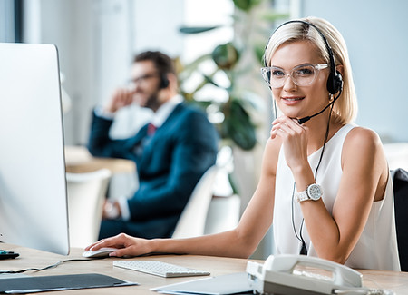 selective focus of cheerful blonde operator in headset looking at camera .jpg