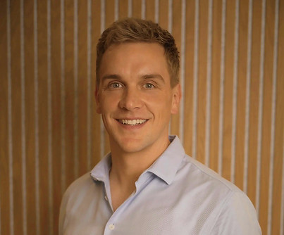 Portrait of Tom Dixon, physiotherapist at SYNC Therapies, photographed against warm timber slats.