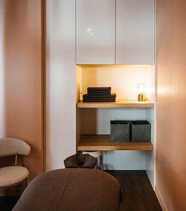 Calm treatment room at SYNC Therapies featuring a massage table, soft peach walls and neatly arranged shelving with warm ambient lighting.