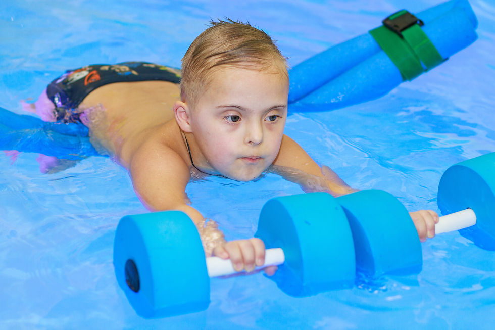 A young boy with wet blond hair with Down's Syndrome in a pool floating on foam training swimmes' weights.