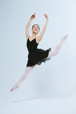 Image description: A ballerina performs in a black dress and pink pointe shoes against a minimalist background.