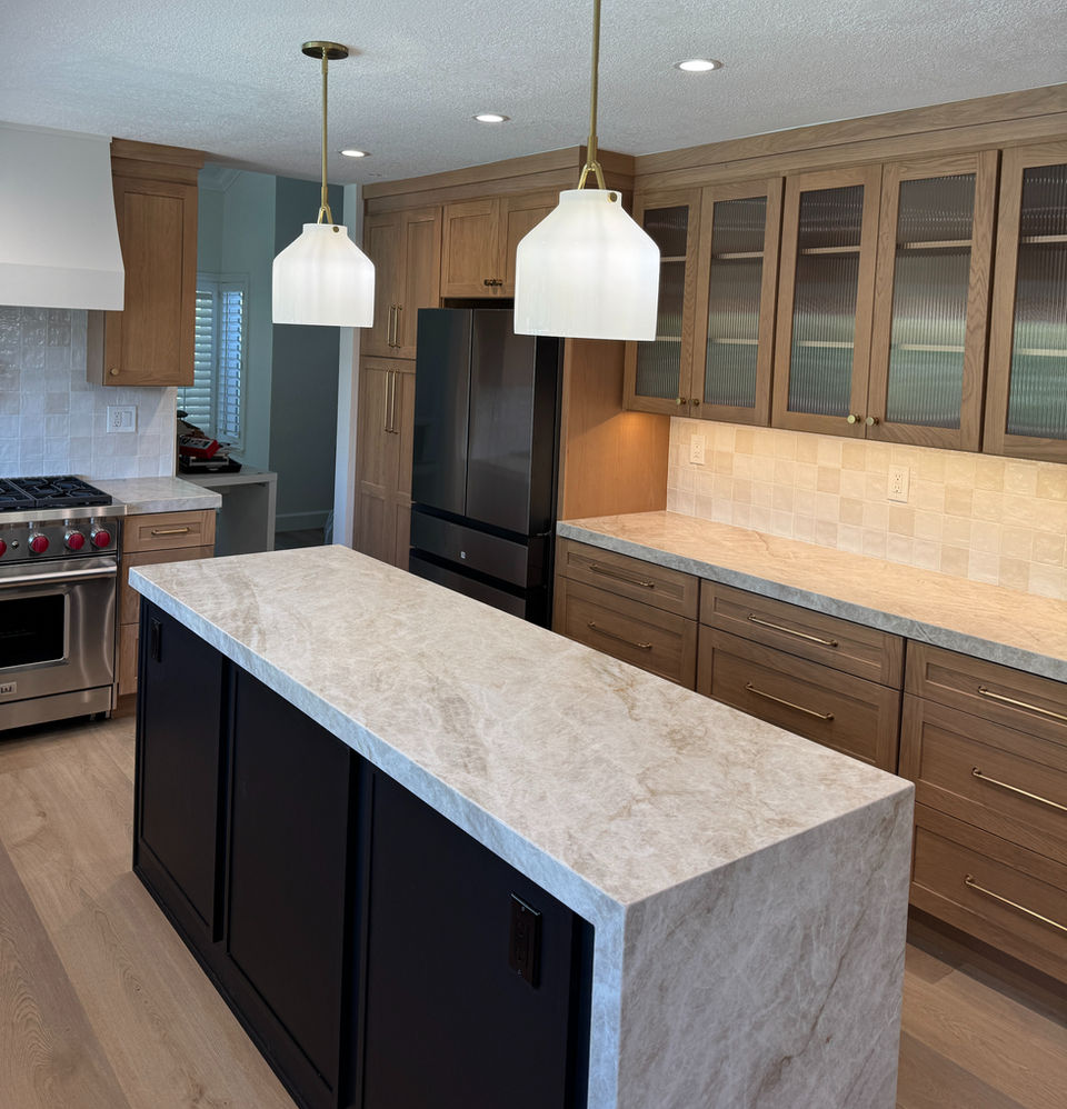 Modern kitchen with large island, light wood cabinets, and black appliances.
