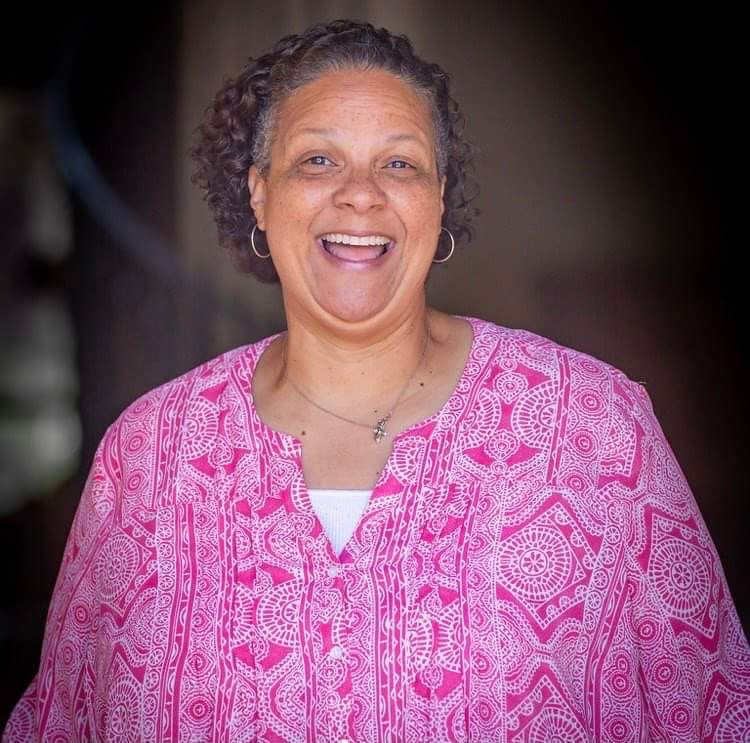 Woman smiling brightly in a patterned pink top, reflecting the joyful and welcoming spirit of Laughter for All community events.
