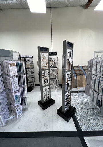 Modern kitchen showroom display with dark grey shaker cabinets, a large white quartz island with a built-in black cooktop, stainless steel refrigerator, and a white apron sink.