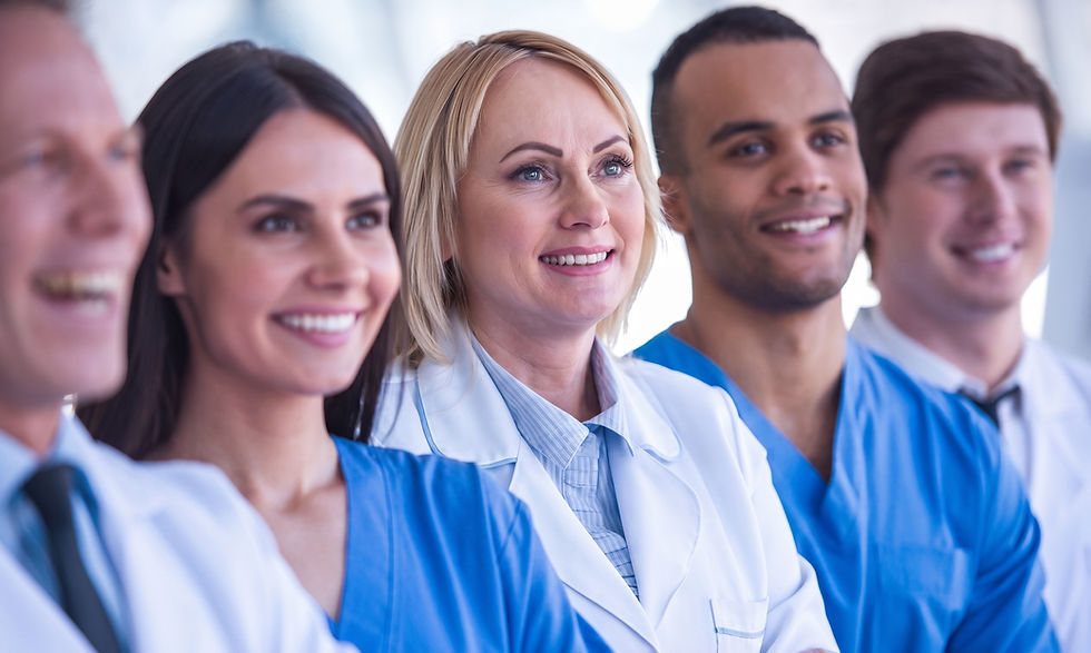 Four smiling medical professionals in scrubs and lab coats stand confidently in a modern, bright building
