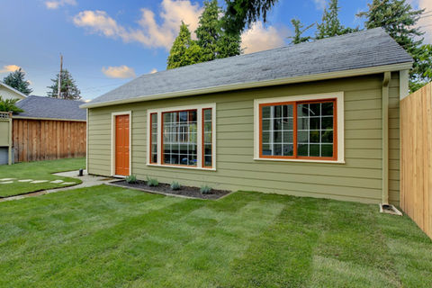 Green home exterior with windows and door against a blue sky background.