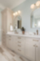 Elegant bathroom with light fixtures, mirrors, cabinets, and a potted plant.