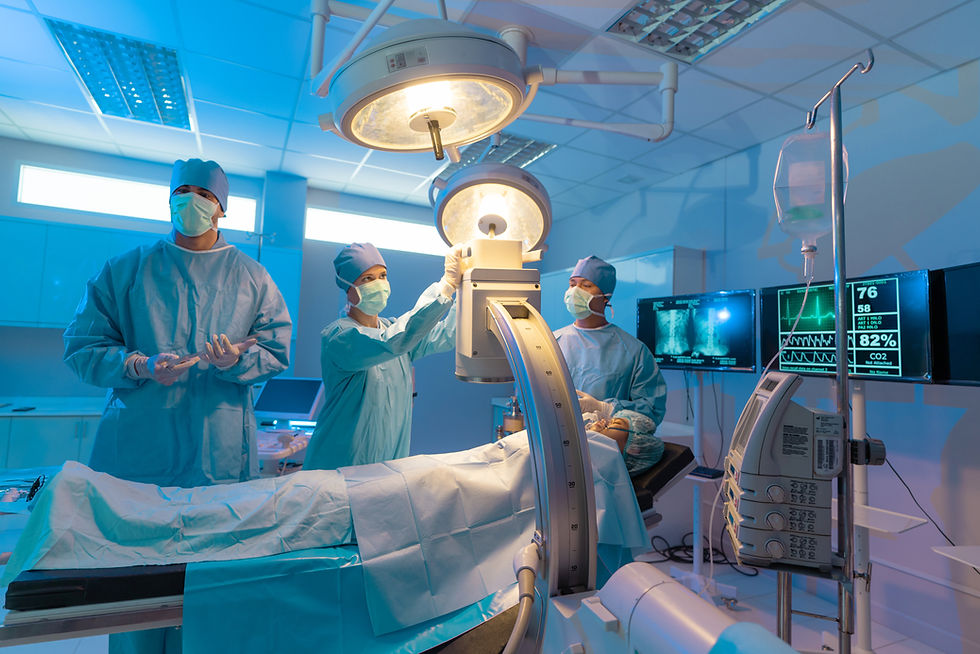 Doctors in blue scrubs and masks operate under bright surgical lights. Medical monitors display vital signs. Operating room setting.