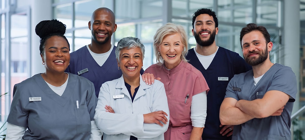 Six smiling healthcare professionals in scrubs pose in a bright medical office. Name tags visible; two wear white coats. Mood is cheerful.