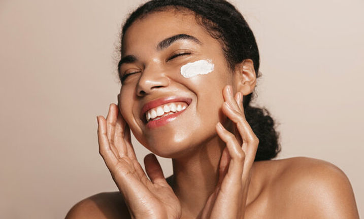 Smiling woman applying skincare cream, promoting radiant and healthy skin results at Azira Aesthetics.