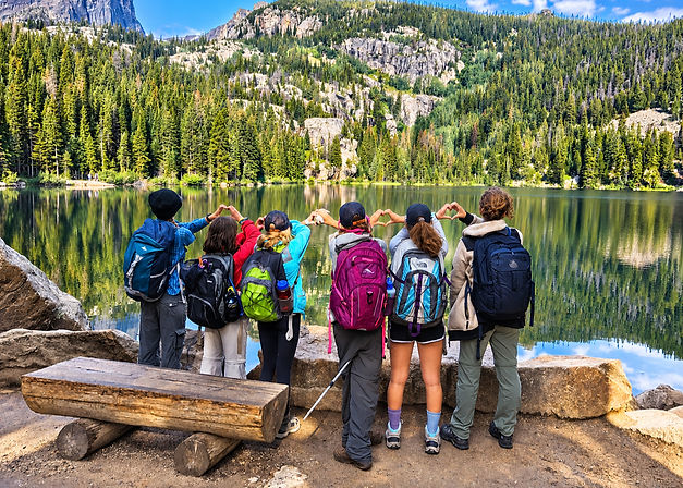 Group of young hikers making heart shapes with their hands beside a Colorado alpine lake during an outdoor adventure.