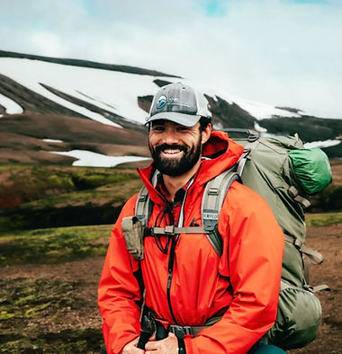 XPAdventure outdoor adventure guide wearing a red jacket and expedition backpack in an alpine mountain setting.
