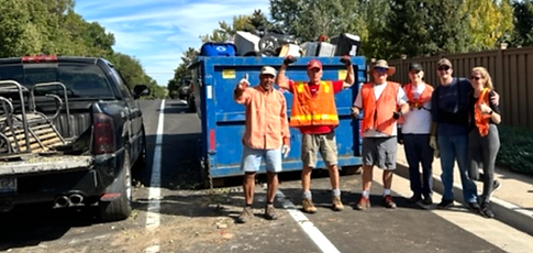 Volunteer members celabrating in front of trash dumpster full of trash. 