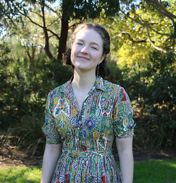 A portrait of Diverse & Thriving's admin assistant Emma Hearnes. She wears a colourful dress against a background of greenery
