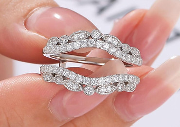 Close-up of a person holding a diamond-encrusted curved white gold ring between fingers.