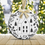 Miniaturbild: Rundes Weihnachtsornament mit verschneitem Haus, umgeben von Tannenzweigen und Weihnachtsdekoration.