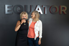 photo of two blonde women - one is drinking a coffee and the other is looking at her and smiling