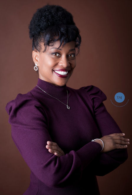 Beautiful Black female CEO of a Coffee Company, poses for a professional headshot wearing a plum colored sweater against a coffee colored background.
