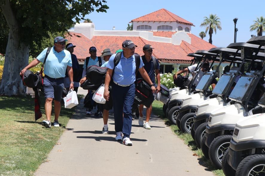 Wide-angle view of golfers gathering near the first tee at a sunny charity tournament.