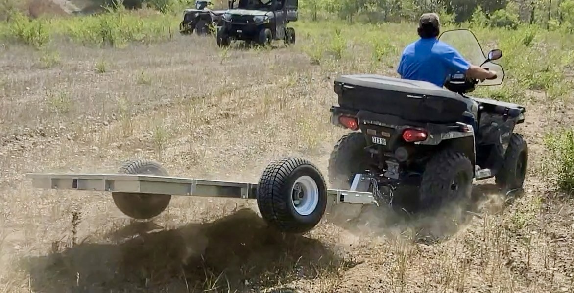 Rambo Trailer, an aluminium multi-use on and off road trailer being field tested in a dusty field behind a four wheeler. 