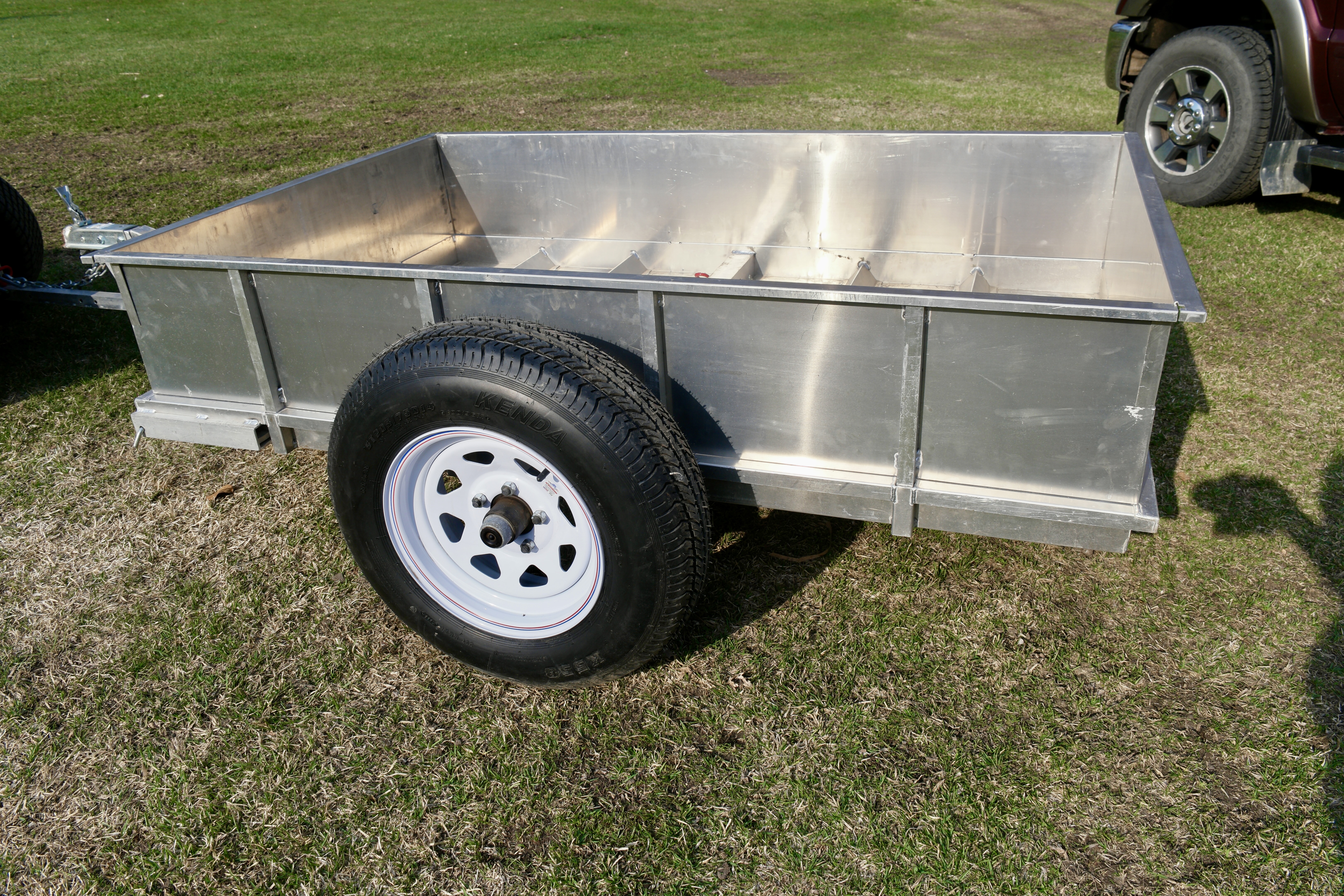 Rambo Trailer, an aluminium multi-use on and off road trailer, parked in the grass with tires on it. 