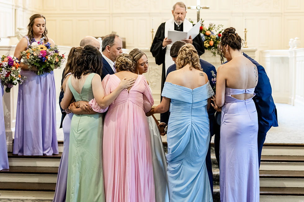 A faith-filled wedding moment with parents and siblings gathered in prayer around the bride and groom at the altar.