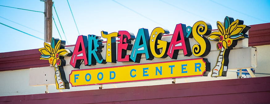 Arteaga's Food Center sign with colorful lettering, palm tree decor, under a blue sky.