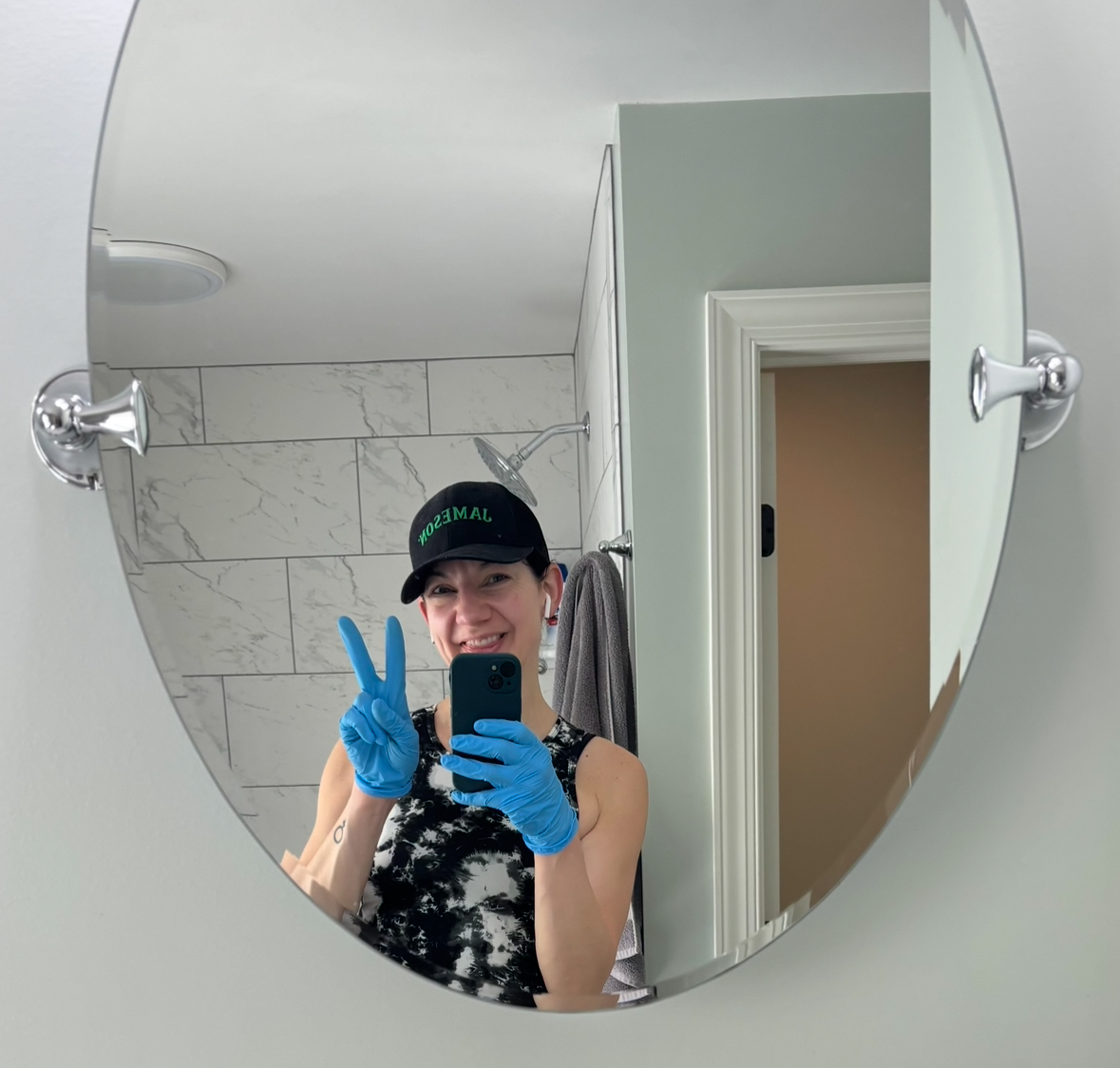 Jen smiling and taking a selfie while cleaning a bathroom, holding up a peace sign