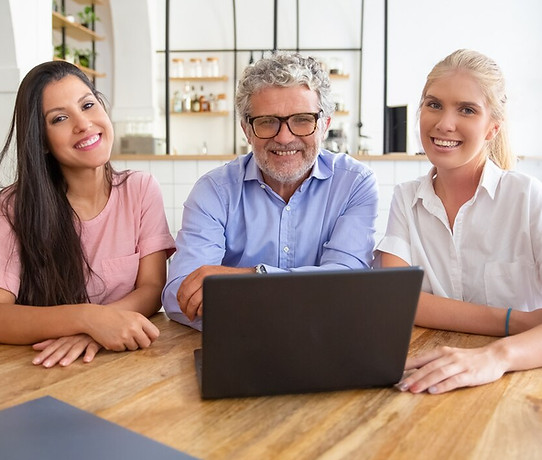 happy-successful-business-team-sitting-table-with-open-laptop-looking-camera-posing-smilin