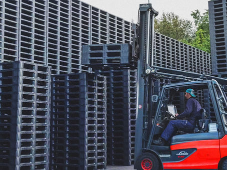 Truck lifting up plastic pallets on stack of plastic pallets, big stacks of black plastic pallets in background