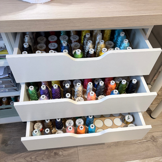 Bobines de fils à broder aux couleurs naturelles disposées sur une étagère dans l’atelier de broderie machine.