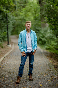 High school senior boy in blue shirt and jeans in woods