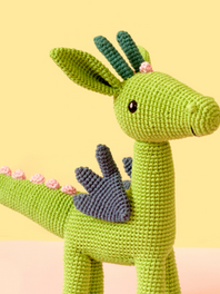 A imagem mostra um dragão verde feito de crochê. 